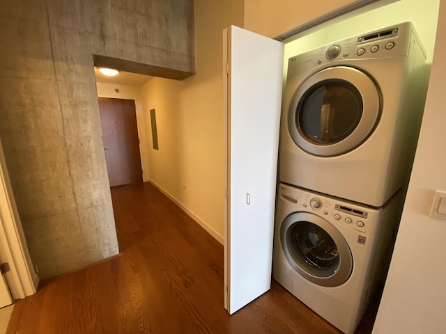 laundry area with laundry area, electric panel, baseboards, dark wood-style flooring, and stacked washing maching and dryer