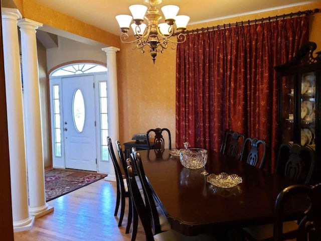 dining room with a healthy amount of sunlight, wood finished floors, an inviting chandelier, and decorative columns