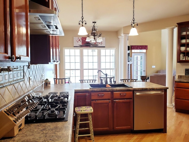 kitchen featuring black gas stovetop, stainless steel dishwasher, hanging light fixtures, ornate columns, and a sink