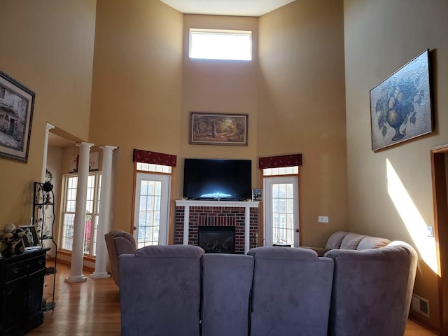 living area featuring wood finished floors, visible vents, ornate columns, a high ceiling, and a fireplace