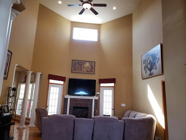 living area featuring a ceiling fan, wood finished floors, a high ceiling, a fireplace, and decorative columns