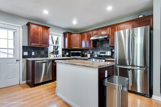 kitchen featuring under cabinet range hood, a center island, appliances with stainless steel finishes, decorative backsplash, and light wood finished floors