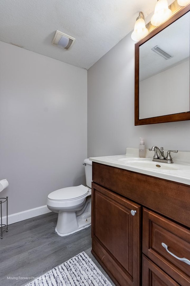 bathroom with toilet, vanity, wood finished floors, and visible vents