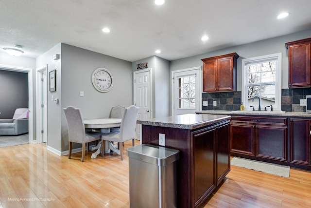 kitchen with light wood-type flooring, tasteful backsplash, a kitchen island, and a sink