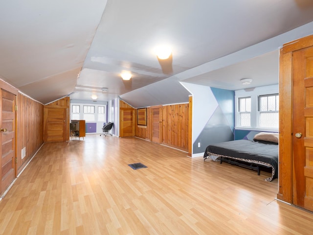 bonus room with vaulted ceiling, wooden walls, light wood-style flooring, and visible vents