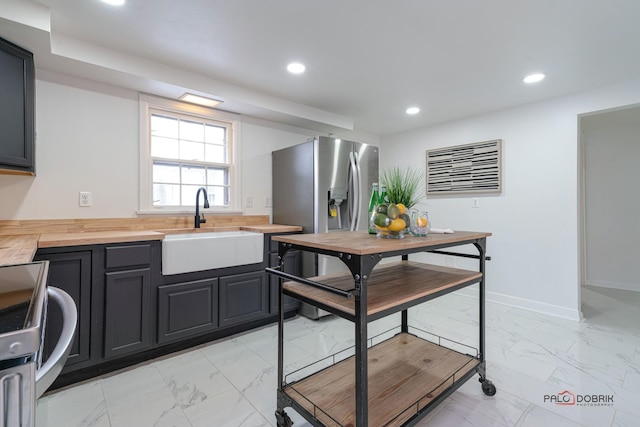 kitchen with marble finish floor, wood counters, stainless steel refrigerator with ice dispenser, and a sink