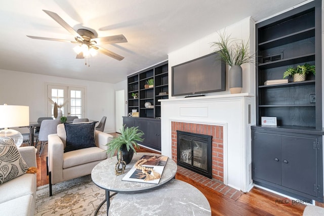 living room featuring a fireplace, wood finished floors, a ceiling fan, and built in features