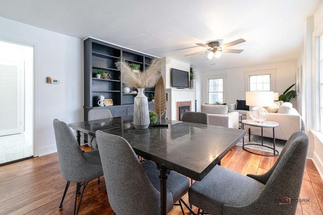 dining space featuring a brick fireplace, baseboards, a ceiling fan, and hardwood / wood-style floors