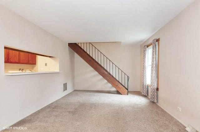 unfurnished living room featuring visible vents, stairs, and carpet