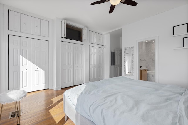 bedroom featuring light wood finished floors, two closets, visible vents, ensuite bathroom, and ceiling fan