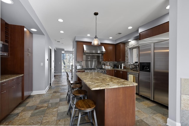 kitchen featuring stone tile floors, stainless steel appliances, baseboards, decorative backsplash, and wall chimney exhaust hood