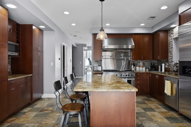 kitchen featuring a sink, visible vents, high quality appliances, wall chimney exhaust hood, and stone finish floor