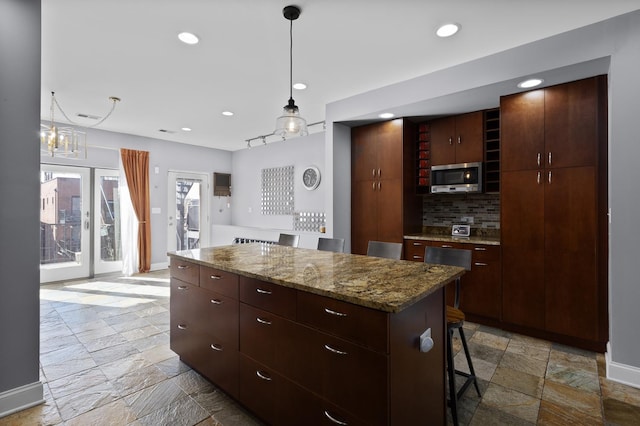 kitchen featuring stone tile floors, decorative backsplash, a kitchen island, stainless steel microwave, and recessed lighting