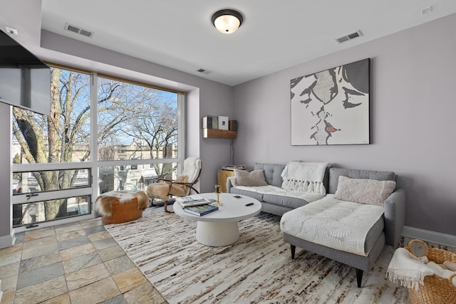 living room with stone tile floors, visible vents, and baseboards