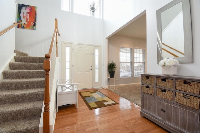 foyer featuring light wood-type flooring, baseboards, a high ceiling, and stairway