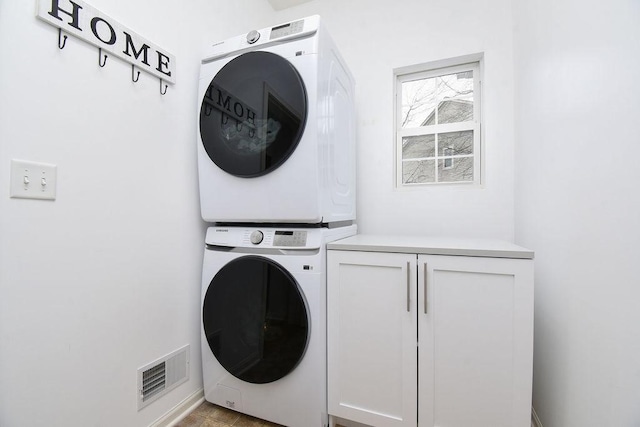 laundry room with cabinet space, visible vents, and stacked washer and clothes dryer