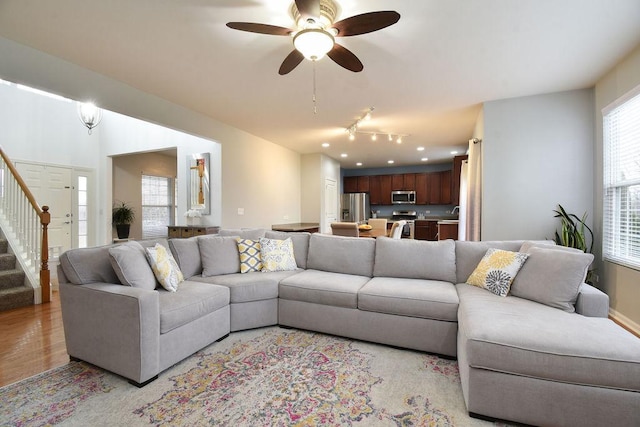 living room with stairs, a ceiling fan, and light wood-style floors