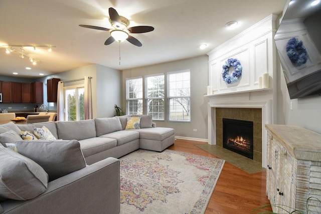 living room featuring light wood-type flooring, a healthy amount of sunlight, a ceiling fan, and a tiled fireplace