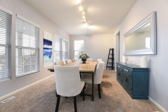 dining space featuring rail lighting, baseboards, visible vents, and light colored carpet