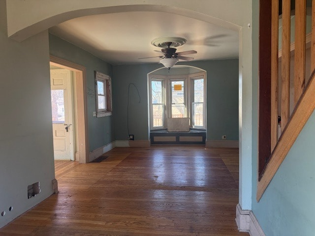 entrance foyer featuring arched walkways, wood finished floors, a ceiling fan, and baseboards