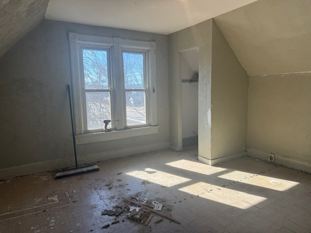 additional living space featuring a textured wall and vaulted ceiling