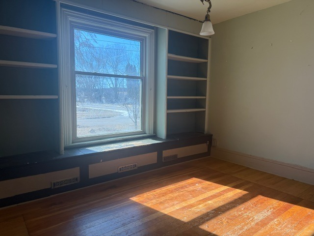 empty room with built in shelves, hardwood / wood-style floors, a wealth of natural light, and baseboards