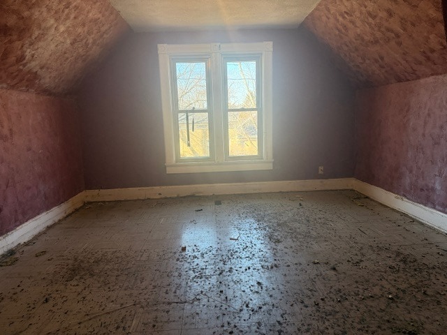 additional living space featuring lofted ceiling, a textured ceiling, and baseboards