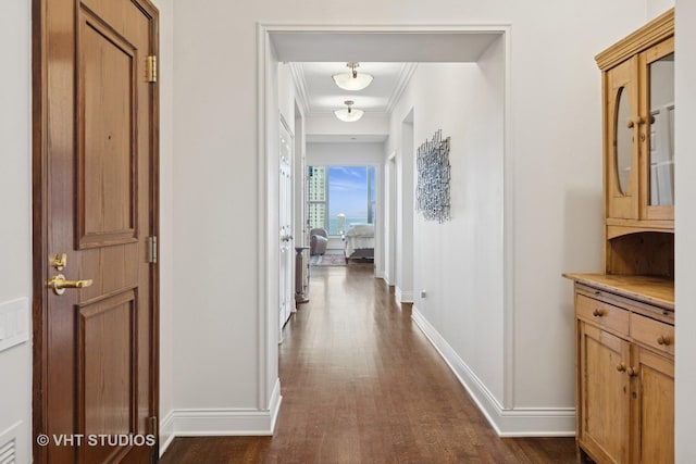 hallway featuring dark wood finished floors, crown molding, and baseboards