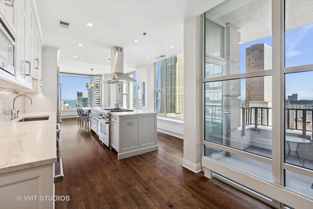 kitchen featuring visible vents, a sink, white cabinets, high end stainless steel range oven, and island range hood