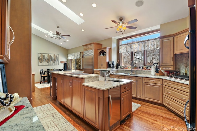 kitchen featuring an island with sink, stainless steel appliances, vaulted ceiling with skylight, light wood-style floors, and light stone countertops