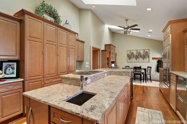 kitchen with a center island with sink, vaulted ceiling with skylight, recessed lighting, wood finished floors, and a sink