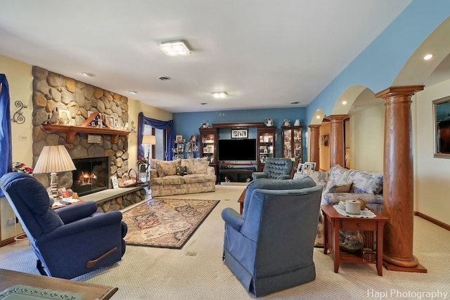 living area featuring arched walkways, carpet, a stone fireplace, baseboards, and ornate columns