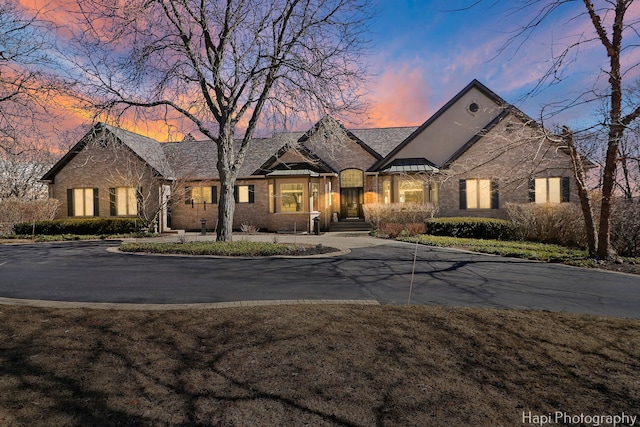 french country style house featuring metal roof, brick siding, driveway, and a standing seam roof