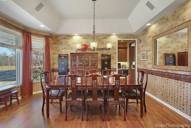 dining space with wallpapered walls, a raised ceiling, and wood finished floors