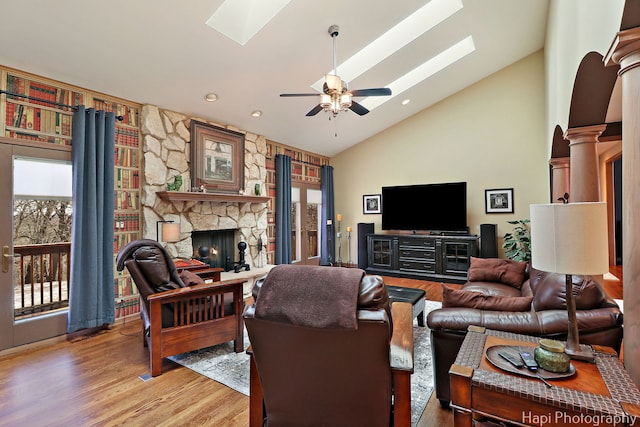 living room with a ceiling fan, a skylight, a fireplace, light wood finished floors, and decorative columns