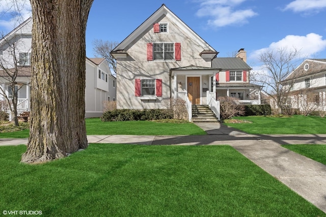 view of front facade with a standing seam roof, a front yard, metal roof, and a chimney