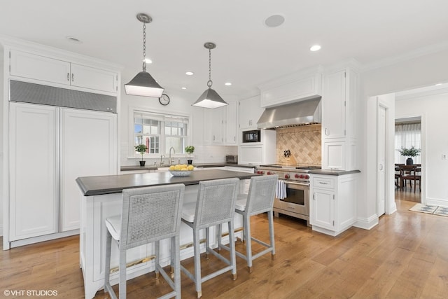 kitchen with built in appliances, dark countertops, wall chimney exhaust hood, and white cabinetry