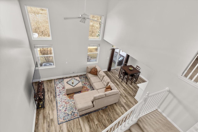 living area with wood finished floors, baseboards, a ceiling fan, stairs, and a towering ceiling