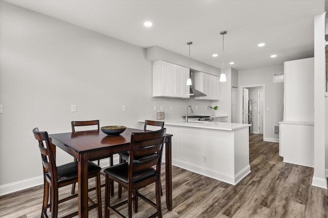 kitchen with dark wood-style floors, a peninsula, wall chimney exhaust hood, and light countertops