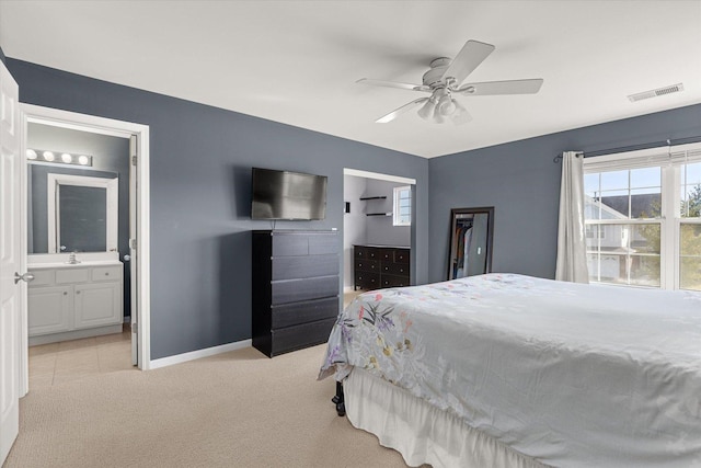 bedroom featuring visible vents, light carpet, ensuite bath, baseboards, and ceiling fan