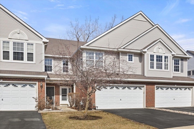 view of property featuring brick siding, driveway, a garage, and roof with shingles