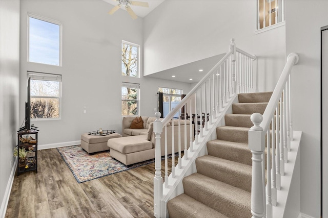 stairway with baseboards, a high ceiling, a healthy amount of sunlight, and wood finished floors