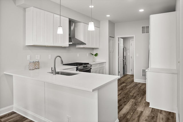 kitchen with visible vents, dark wood-type flooring, a sink, wall chimney range hood, and stainless steel range with gas stovetop