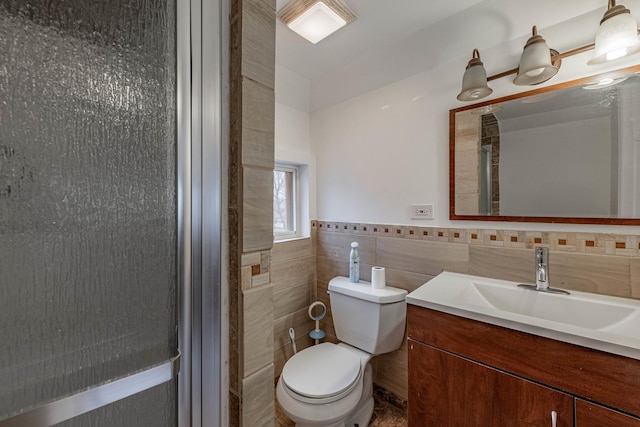 bathroom featuring toilet, a wainscoted wall, tile walls, and vanity