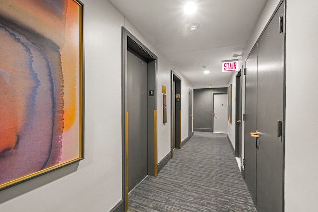 hallway featuring dark colored carpet, elevator, and baseboards