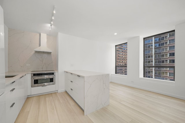 kitchen featuring stainless steel oven, white cabinets, range hood, decorative backsplash, and modern cabinets