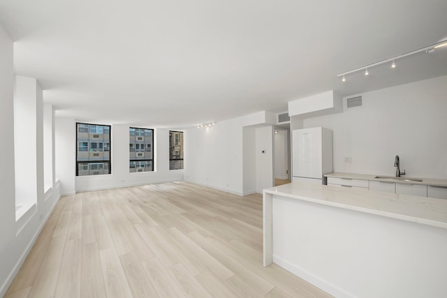 unfurnished living room with light wood-type flooring, a sink, visible vents, and rail lighting