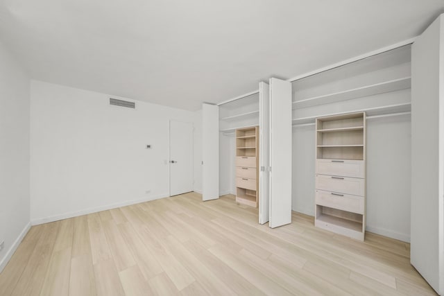 unfurnished bedroom with baseboards, light wood-style flooring, visible vents, and multiple closets