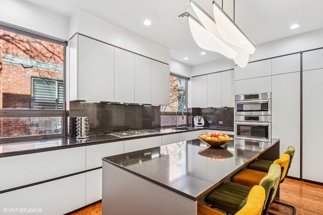 kitchen with a sink, appliances with stainless steel finishes, white cabinetry, dark countertops, and modern cabinets