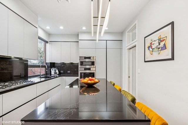 kitchen featuring double oven, dark countertops, backsplash, and a sink